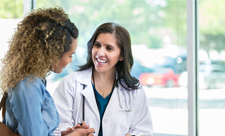 Caring mature female doctor shows test results to a young adult female patient. The doctor is smiling while talking with the patient.