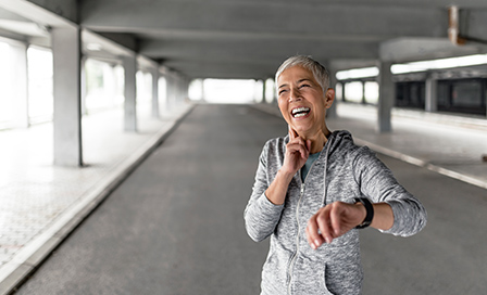 Mature, gray hair woman checking results after jog in the park. Attractive looking mature, short hair female keeping fit and healthy. Joyful senior lady using tracker after exercising. Runner checking pulse after exercising with her smart watch. Smiling runner checking heart rate after exercising. Concept sport and fitness