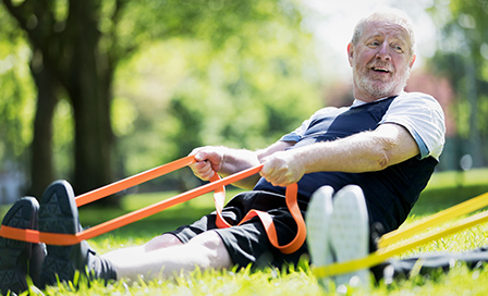 Active senior man exercising in park, stretching with resistance band