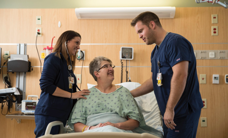 Two nurses standing by a patient's bed in light conversation