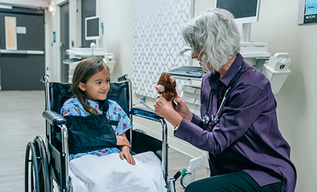 Doctor showing teddy bear to girl in wheelchair