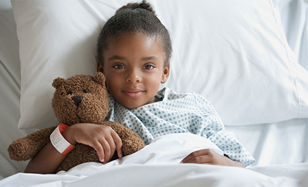 Mixed race girl in hospital bed with teddy bear