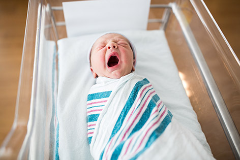 A one-day-old newborn infant yawns in its crib in the hospital.