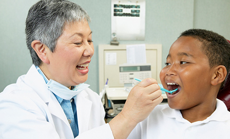 Senior Asian female dentist examining young male patient