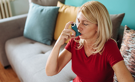 Senior woman in her late 50s inhaling asthmatic cure at home. Woman is living life with chronic illness everyday and overcoming challenges with it.