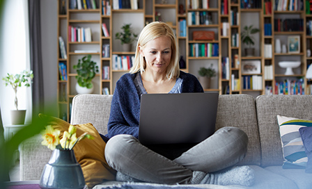 Woman working on a laptop sitting on her couch.